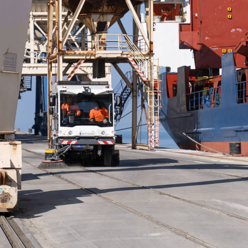 Dulevo D6 straatveegmachine aan het werk op een havenkade bij schepen