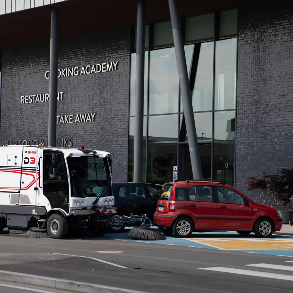 Dulevo D3 straatveegmachine veegt straat bij winkelgebied met verkeer