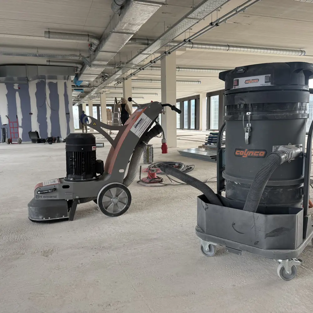 Coynco Iclean 350 met zichtbaar logo naast vloerschuurmachine op bouwplaats