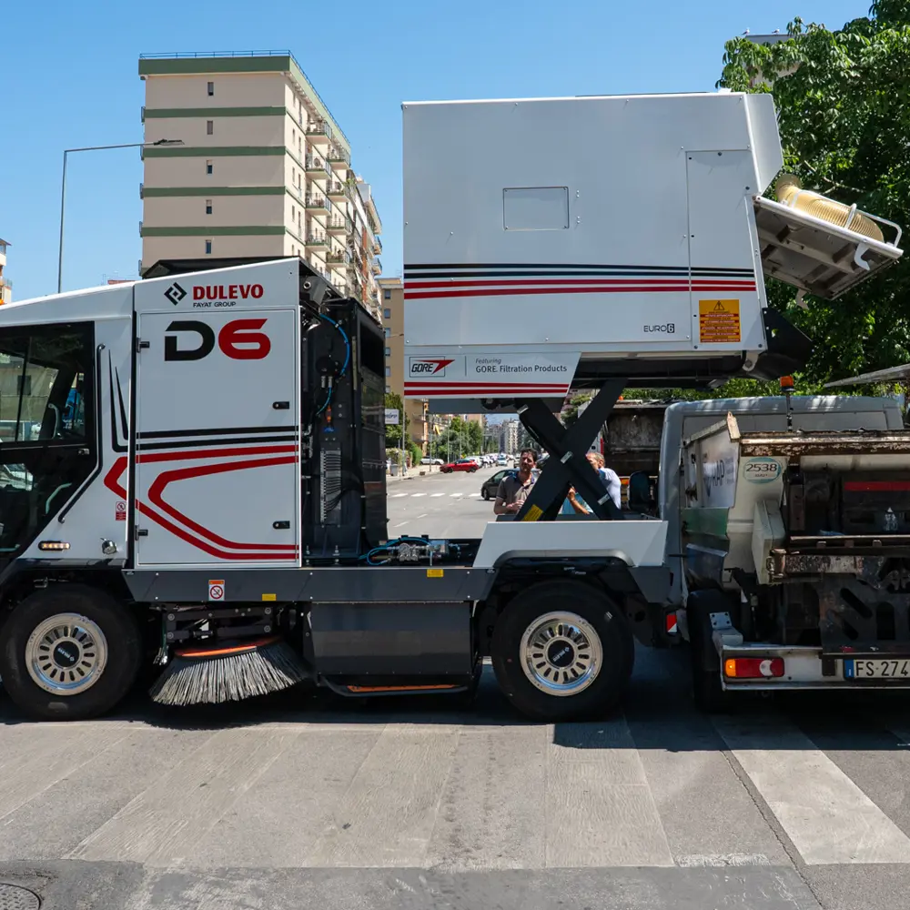 Dulevo D6 veegmachine in actie op een stadsstraat naast vuilniswagen