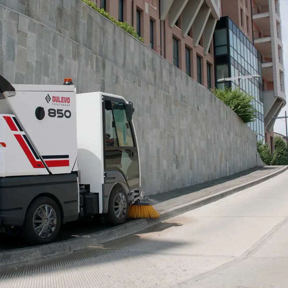 Dulevo 850 veegkar veegt langs betonnen muur naast modern gebouw op brede weg in Nederland