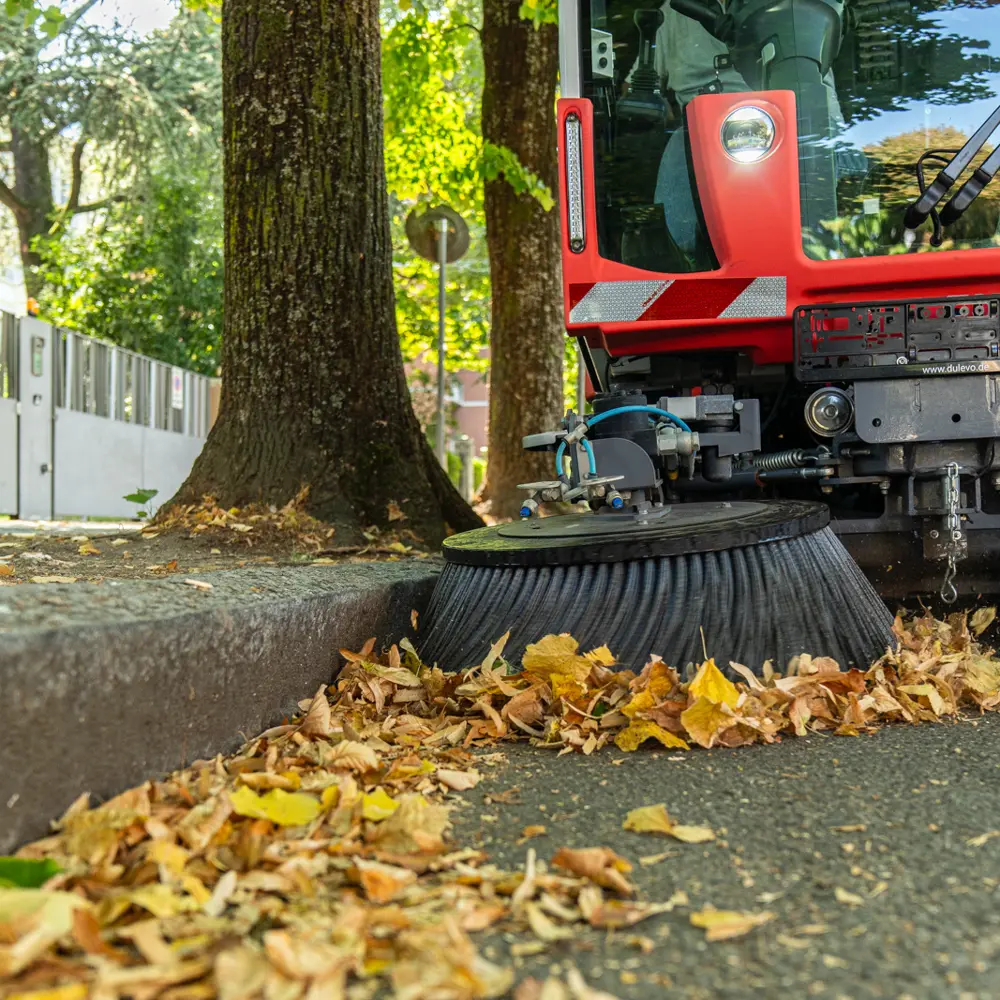 Close-up van zijborstel Dulevo Dzero2 die herfstbladeren van de stoeprand veegt