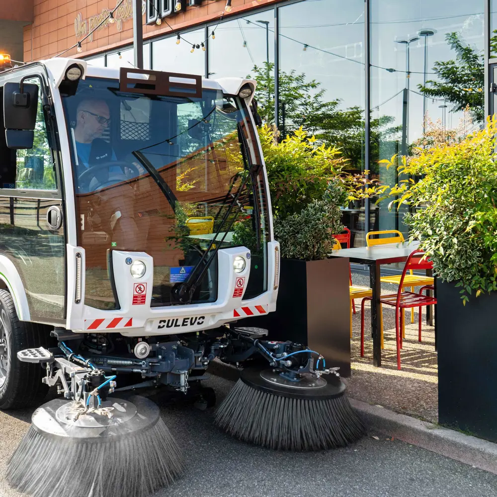 Vooraanzicht Dulevo Dzero2 elektrische straatveegmachine met veegborstels bij winkelgebied