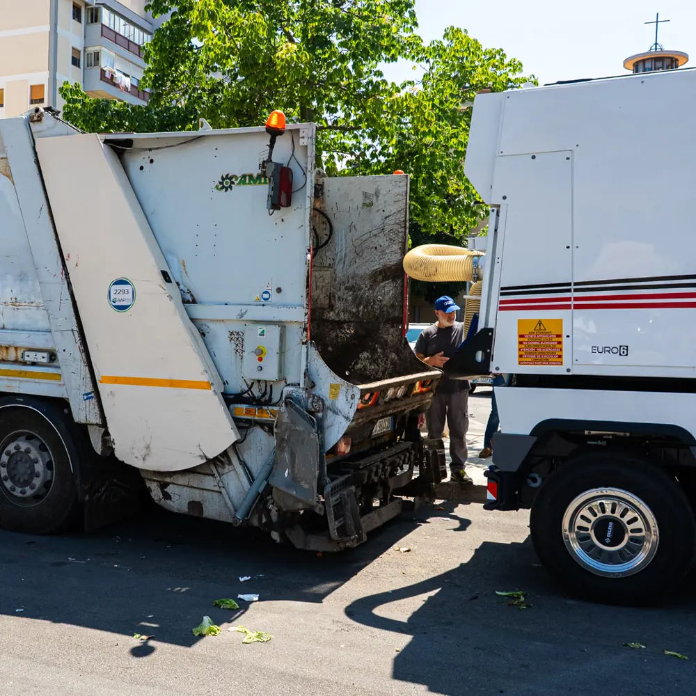 Dulevo D6 veegwagen lost vuil bij een vuilniswagen in de stad